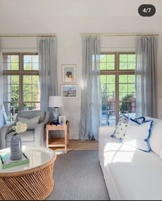 a living room filled with white furniture and lots of window curtains on the windowsill