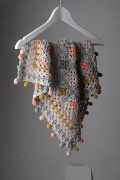 a crocheted shawl hanging on a hanger with pom - poms