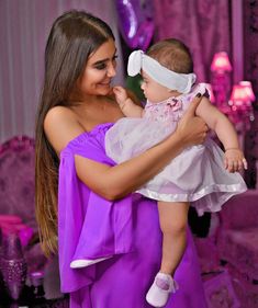 a woman in a purple dress holding a baby wearing a white headband on her head