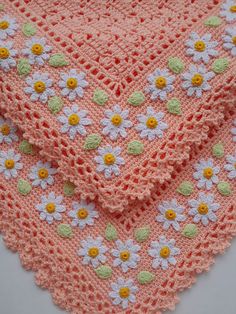 a pink crocheted blanket with white and yellow daisies on the edges, sitting on top of a table