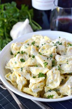 a white bowl filled with pasta covered in cheese and parsley next to wine glasses