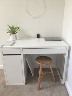 a white desk with a wooden stool in front of it and a potted plant on top