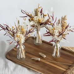 two clear vases with dried flowers on a wooden tray