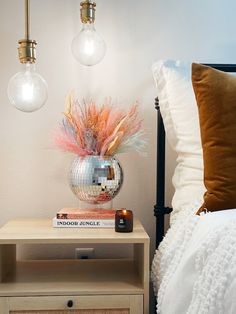 a nightstand with a mirror ball on top and two lights hanging above it next to a bed