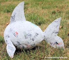 a fish made out of newspaper sitting in the grass