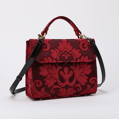 With a nod to the Victorian era, MCW's freshly combines the classic and elegant design of the traditional carpet satchel with a textural and tactile twist. This exquisite top handle satchel is a perfect blend of style and practicality. Spacious interior with zipper and slip pockets, detachable shoulder strap. Sturdy exterior in carpet or velvet, cotton lining. Convenient magnetic flap closure, brass feet for stability. Features: * Detachable, adjustable shoulder strap * Magnetic flap for easy access * Interior slip and zipper pockets * Hand-polished brass hardware * Includes dust bag Dimensions: * Satchel size: 9.50"W x 4"D x 8"H * Adjustable shoulder strap: 43.50" to 51.15" Interior Pockets: * Zipper pocket: 7"W x 5"H * Slip pocket: 8"W x 5.50"H Weight: 1lb 5oz Luxury Red Satchel, Luxury Burgundy Satchel Shoulder Bag, Luxury Burgundy Shoulder Satchel, Luxury Burgundy Rectangular Satchel, Luxury Red Bags With Adjustable Handle, Luxury Burgundy Crossbody Satchel, Luxury Double Handle Satchel As Gift, Elegant Burgundy Flap Bag For Travel, Classic Top Handle Flap Bag For Gift