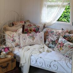 a white bed with lots of pillows on top of it next to a dresser and window