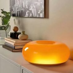 an orange light sitting on top of a white counter next to books and vases