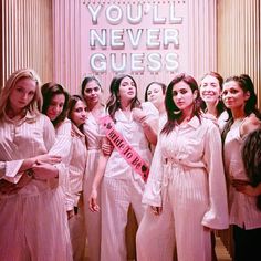 a group of beautiful women standing next to each other in front of a pink sign