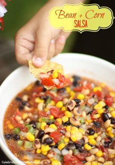 a hand holding a tortilla chip over a bowl of bean and corn salsa