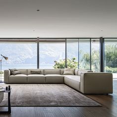 a modern living room with large windows overlooking the water and mountains is furnished with an l - shaped sectional sofa