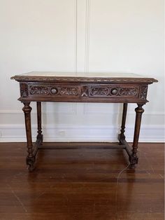 an old wooden table sitting on top of a hard wood floor next to a white wall