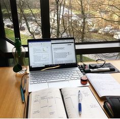 an open laptop computer sitting on top of a wooden desk next to notebooks and pens