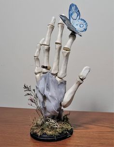 a fake hand holding a blue butterfly on top of a wooden table next to a plant