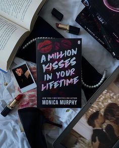 an open book sitting on top of a bed next to other books and makeup items