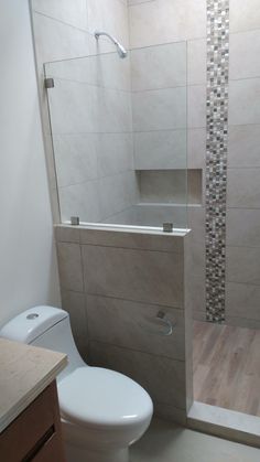 a white toilet sitting next to a shower in a bathroom under a window with tiled walls