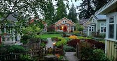 a garden with lots of trees and flowers in front of some small houses on the other side