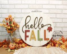 a wooden sign that says hello fall with autumn leaves and flowers in front of a brick wall