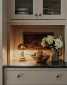 a vase with flowers sitting on top of a kitchen counter next to a bowl of fruit