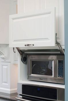 a microwave built into the side of a kitchen wall with white cupboards and drawers