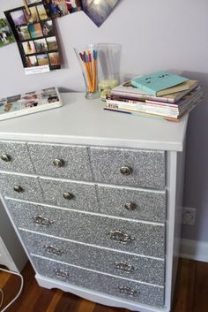 a white dresser with many drawers and pictures on the wall