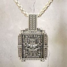 a silver necklace with an intricate design on the front and back sides, sitting on a marble surface