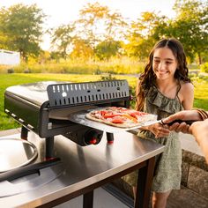 a girl is smiling as she prepares food on an outdoor grill