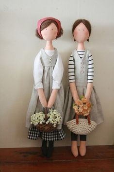 two dolls standing next to each other on a wooden table with flowers in their hands