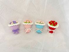 four small crocheted baskets with flowers in them on a white cloth covered surface