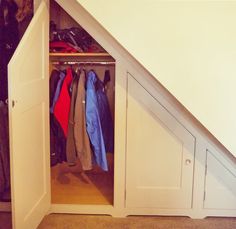 an open closet under the stairs with clothes on hangers