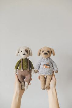 two stuffed dogs in sweaters are being held by someone's hands against a white wall