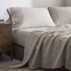 a bed with white sheets and pillows on top of it next to a night stand