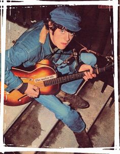 a man sitting on the steps playing a guitar and wearing a blue hat with his hands in his pockets