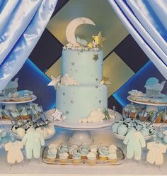 a blue cake with stars and moon decorations on the top is surrounded by cupcakes