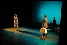 two people standing on a stage with one person holding a suitcase and the other looking at something