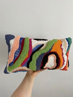 a hand holding up a multicolored pillow