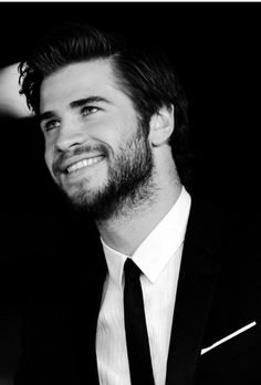 a black and white photo of a man in a suit smiling at the camera with his hand on his hip