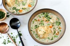 two bowls filled with soup on top of a white table next to wooden spoons