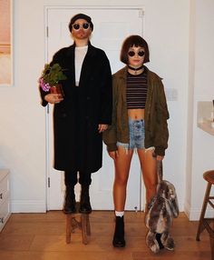 two people standing next to each other in front of a white door and one person holding a potted plant