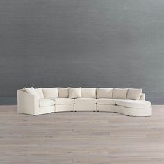 a large white sectional couch sitting on top of a wooden floor next to a gray wall