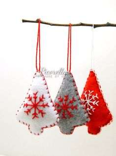 three felt christmas trees hanging from a tree branch with red and white snowflakes on them