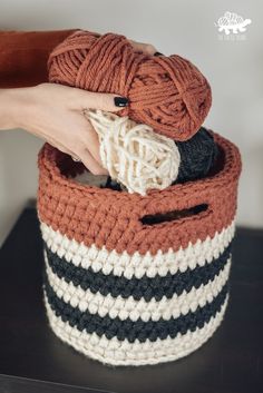 a person holding yarn in a basket on top of a wooden table with black and white stripes