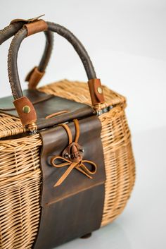 a wicker basket with leather handles and straps on the handle is sitting on a white surface