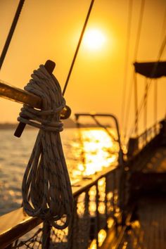 the sun is setting over the ocean on a ship's deck, with ropes tied to it