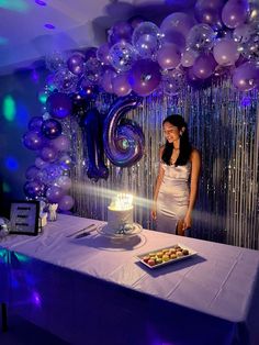 a woman standing in front of a table with a cake and balloons on it at a party