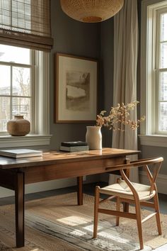 a room with a table, chair and pictures on the wall in front of two windows