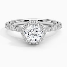 a white gold engagement ring with round diamonds on the band and an oval halo setting