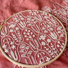 two embroidery hoops sitting on top of a pink cloth covered tablecloth with white embroidered designs