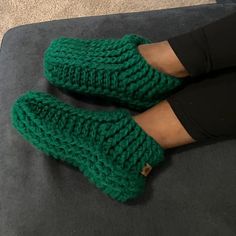 a pair of green knitted slippers sitting on top of a black couch next to a woman's legs