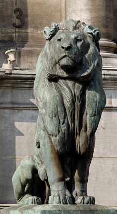 a statue of a lion on top of a stone pedestal in front of a building